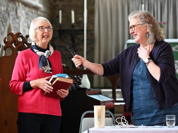 photo of Debbie Young holding a microphone to Ali Bacon, both laughing